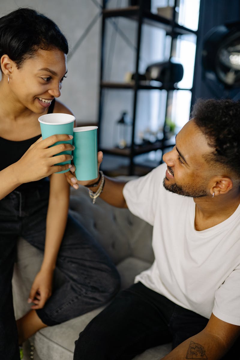 A joyful couple cheers with paper cups while sharing smiles indoors.