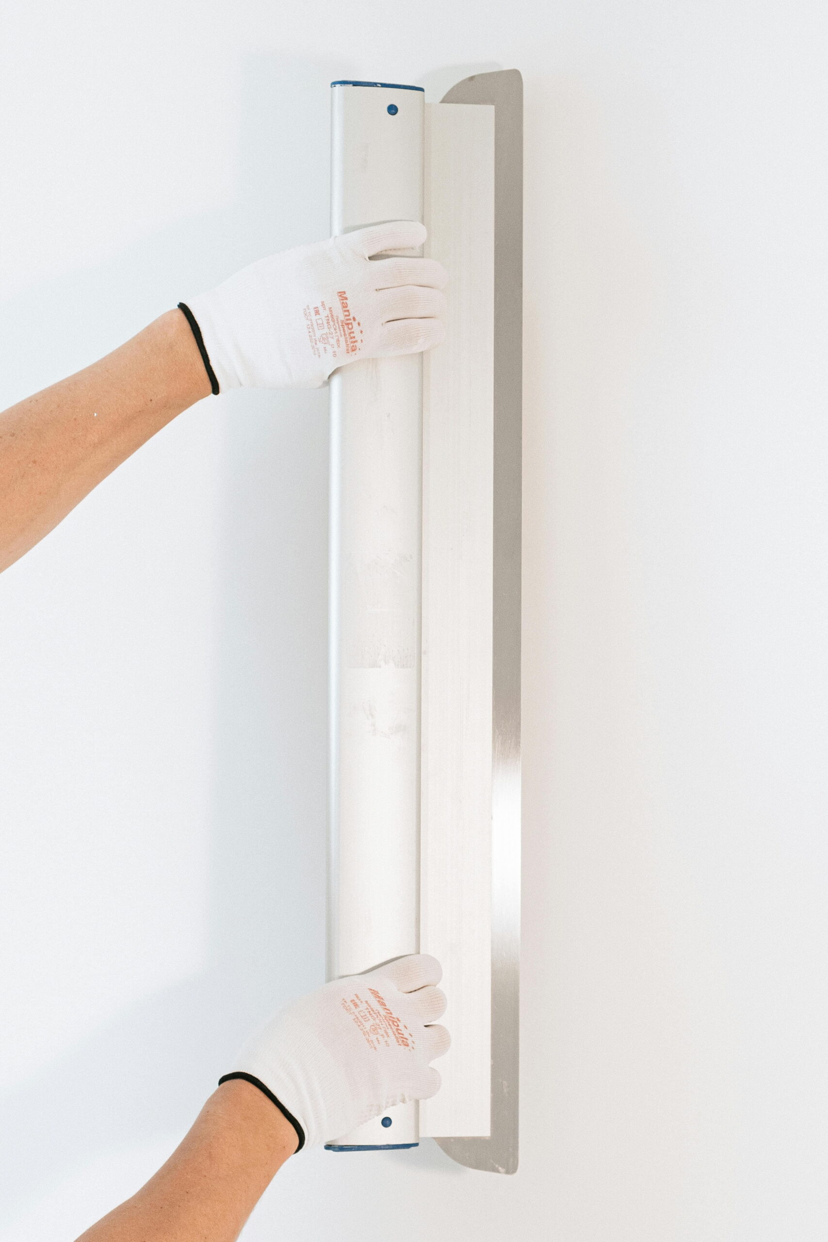 Gloved hands using a trowel to apply and smooth external render, coordinating trades on EWI projects