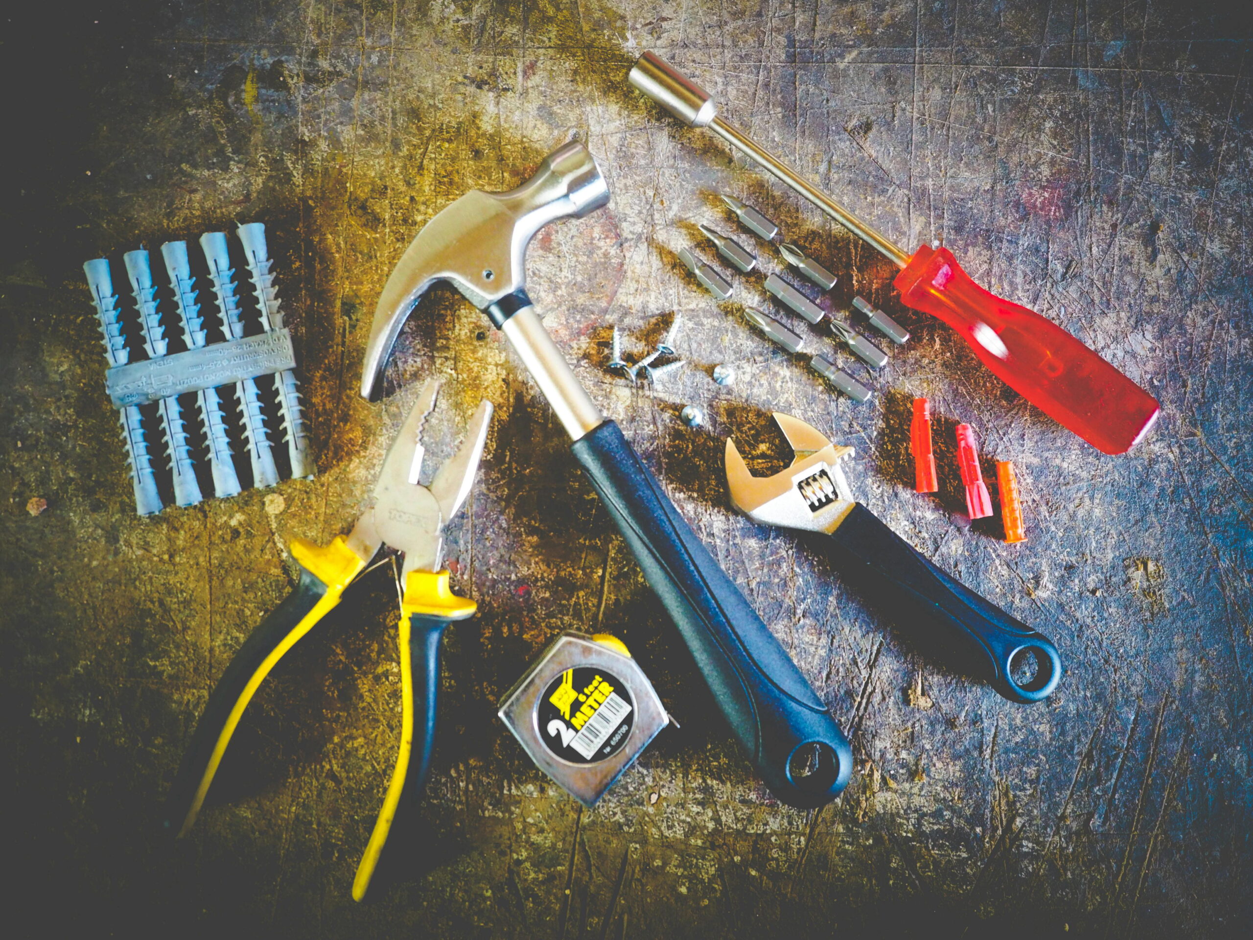 Overhead shot of hand tools including hammer, pliers, adjustable wrench, screwdriver bits, tape measure and wall plugs for Atlas GTA finishing plaster review