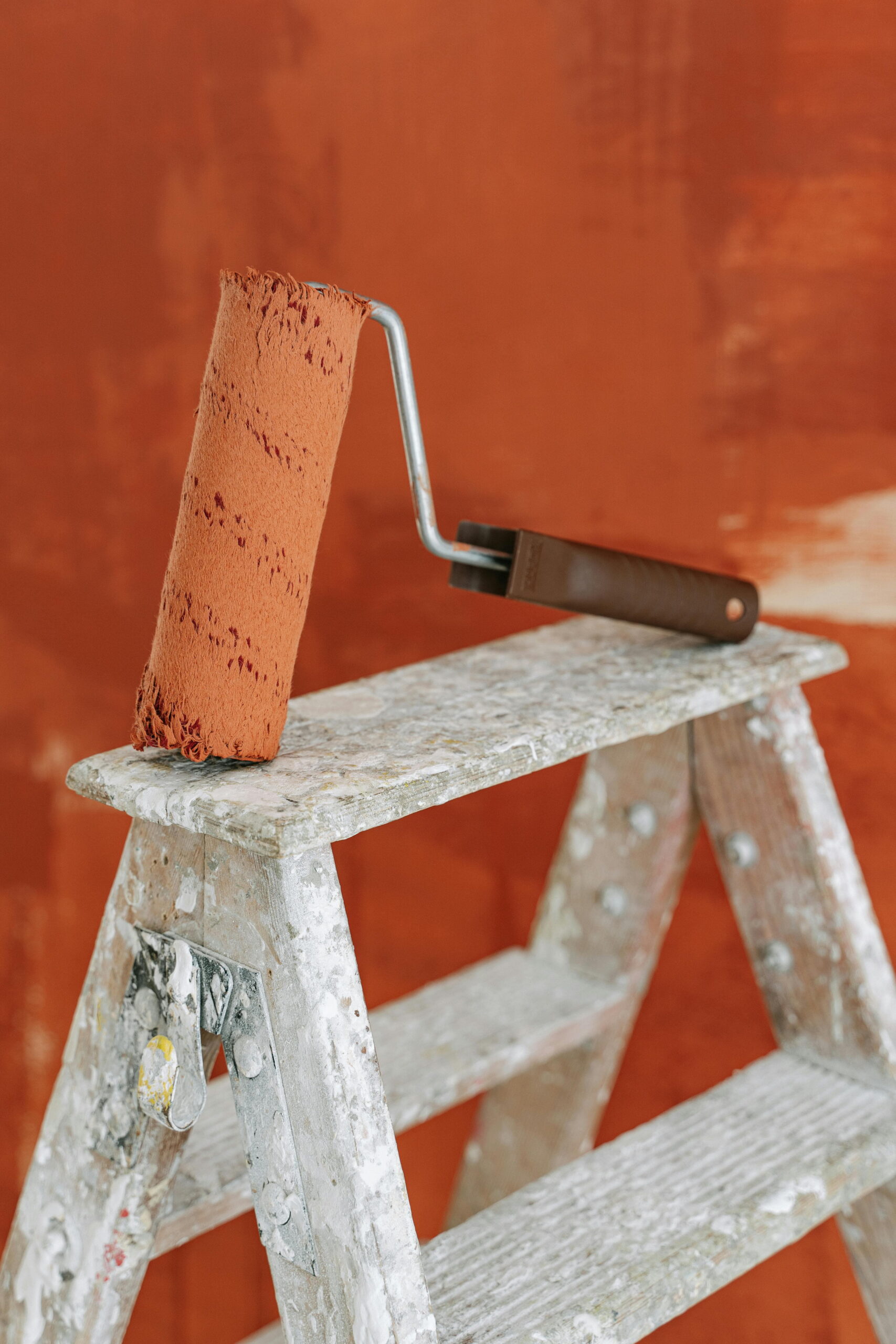Paint roller on ladder applying orange render during seasonal maintenance for rendered walls