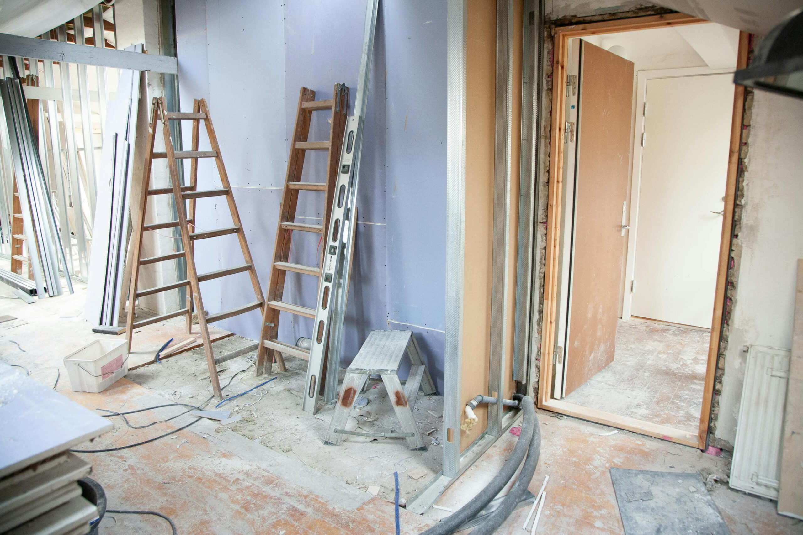 Render paint colour matching process at a renovation site with ladders, metal framing, and plastering materials