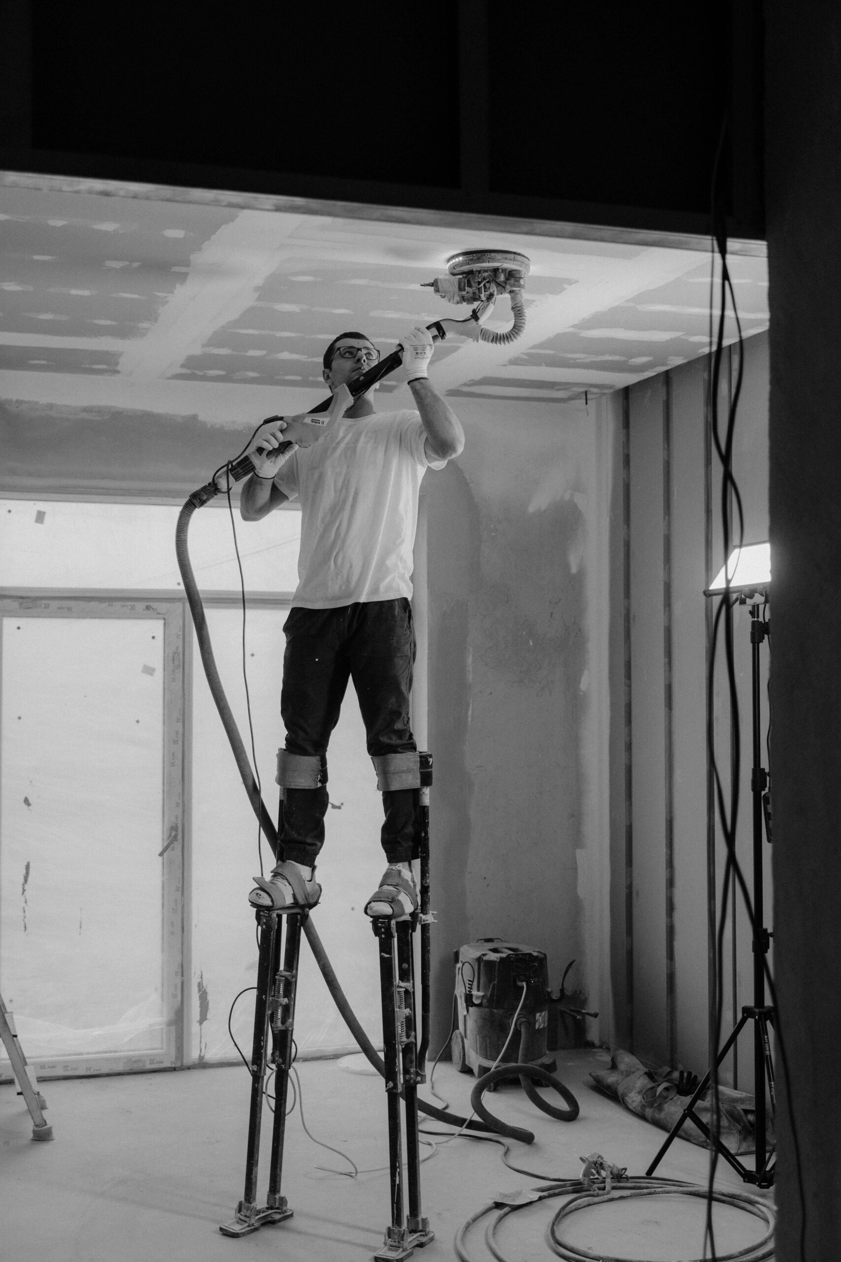 Worker on stilts sanding plaster ceiling using roller frame sizes for render paint