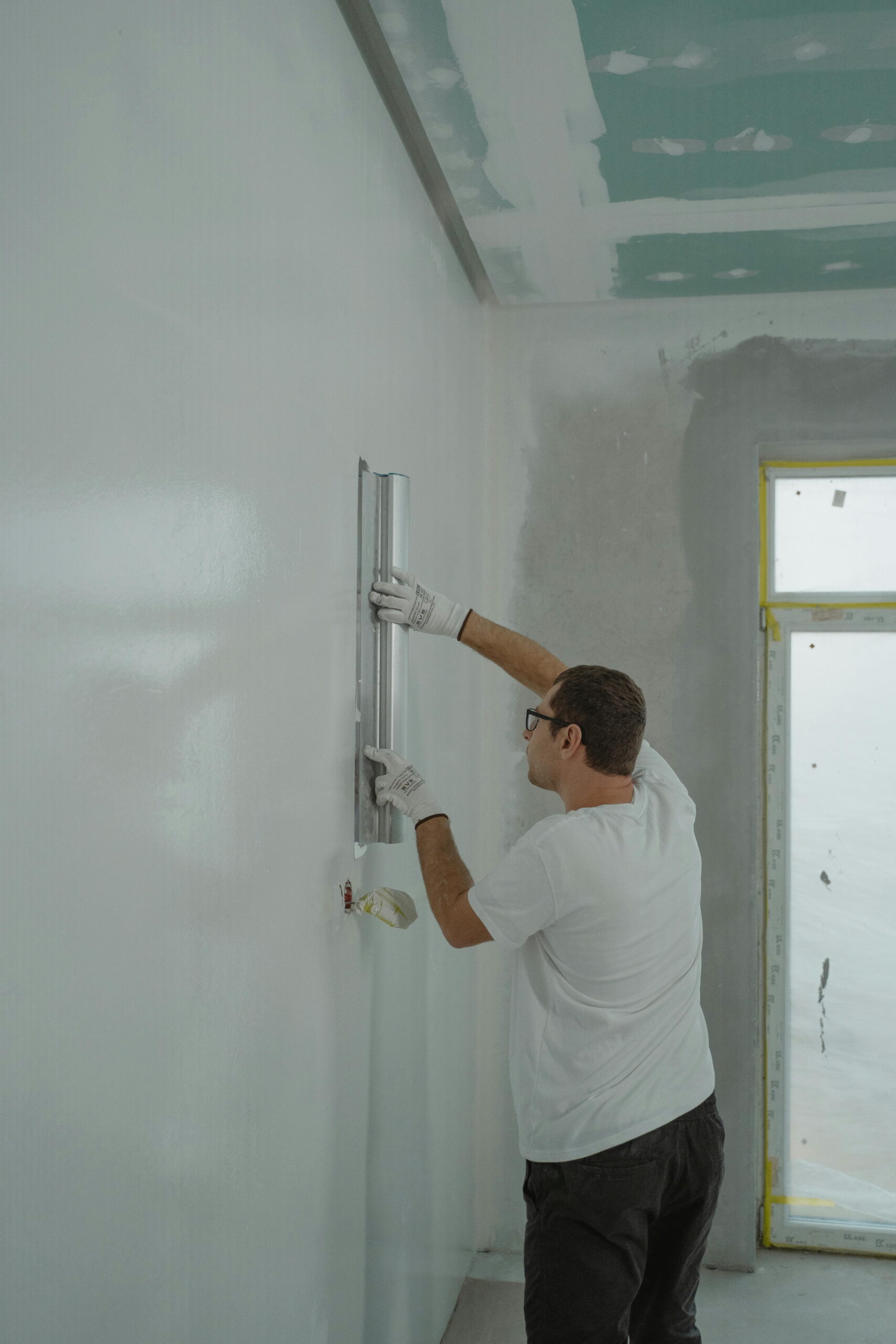 Worker maintaining render on EWI systems using a straight edge on interior wall
