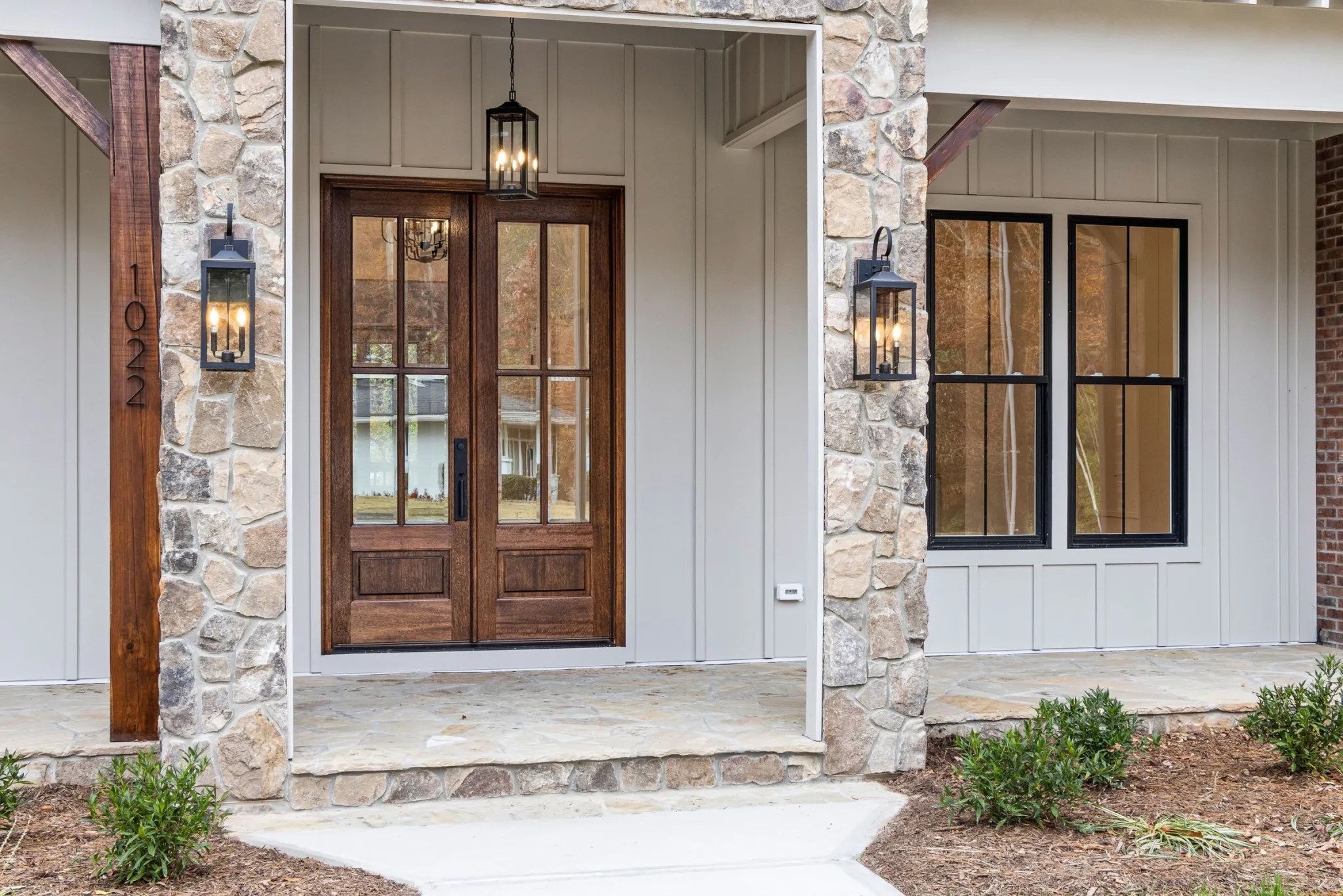 A stone and timber front entry with double doors and lanterns