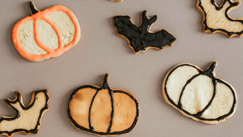 A variety of decorated sugar cookies in the shapes of pumpkins and bats, featuring orange and black icing on a neutral background.