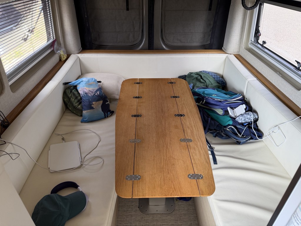 U-shaped lounge below the lift bed, with height-adjustable table; the sides can fold in for easier access