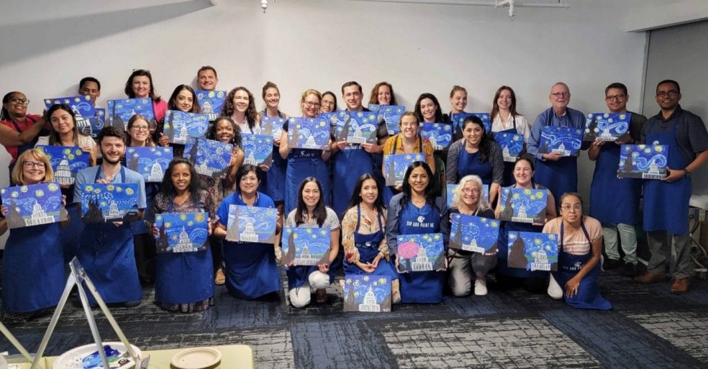 A paint and sip gathering captures a group of people posing with their paintings