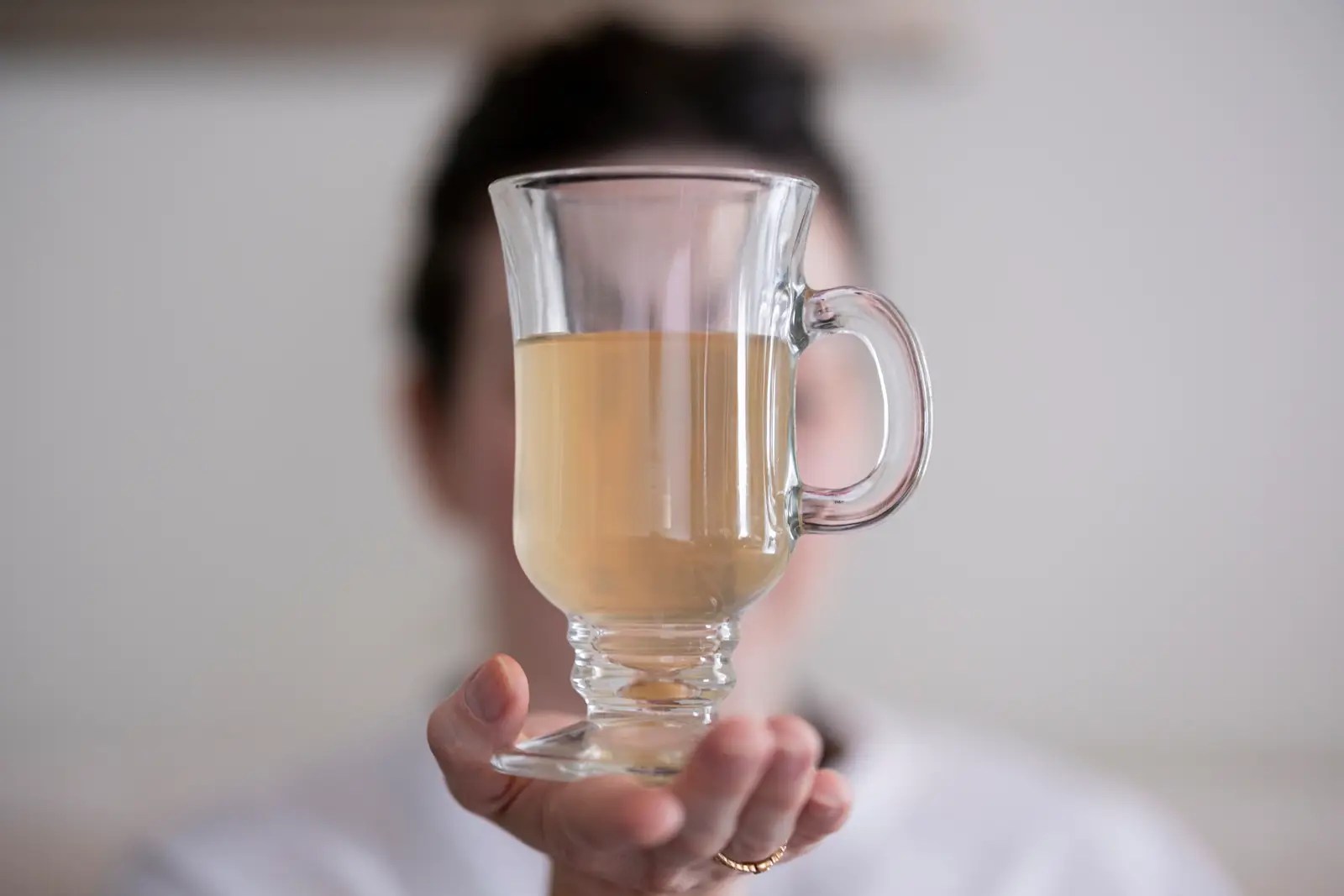 Person holding a transparent glass mug filled with Mulungu tea, a traditional herbal infusion known for its relaxing properties.