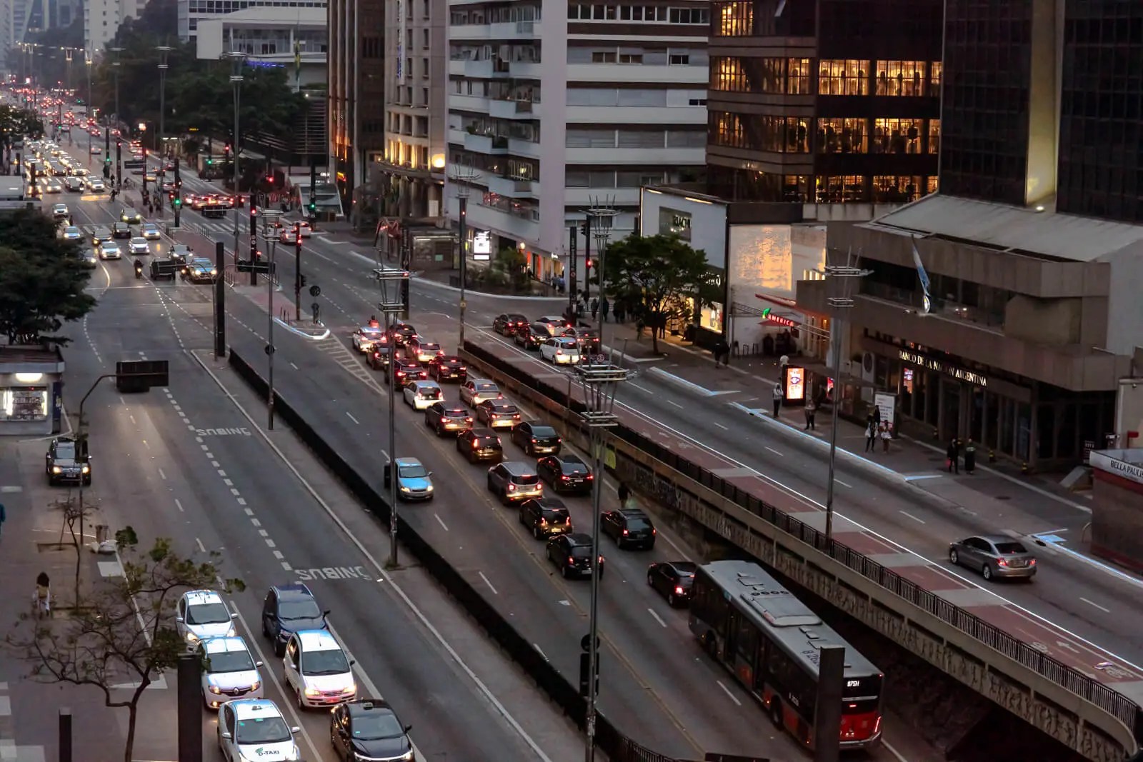 Aerial view of a busy urban avenue at dusk, with rows of cars and people walking among tall buildings - a visual metaphor for the structured and fast-paced rhythm of modern life
