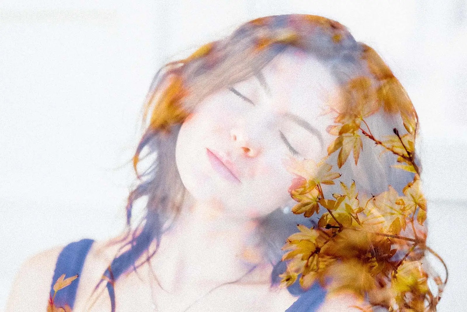Double exposure photograph of a woman with closed eyes blending with golden autumn leaves, symbolizing introspection, identity, and personal growth