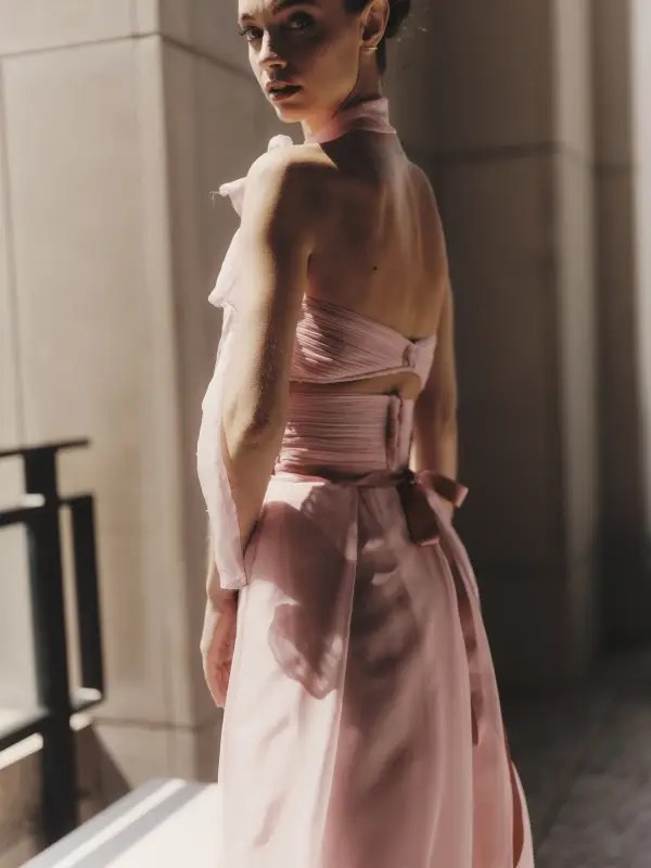 A model stands in golden sunlight wearing the Peony Veil gown, a sculpted Italian silk design with cascading layers and intricate detailing, embodying timeless craftsmanship and ethereal beauty.