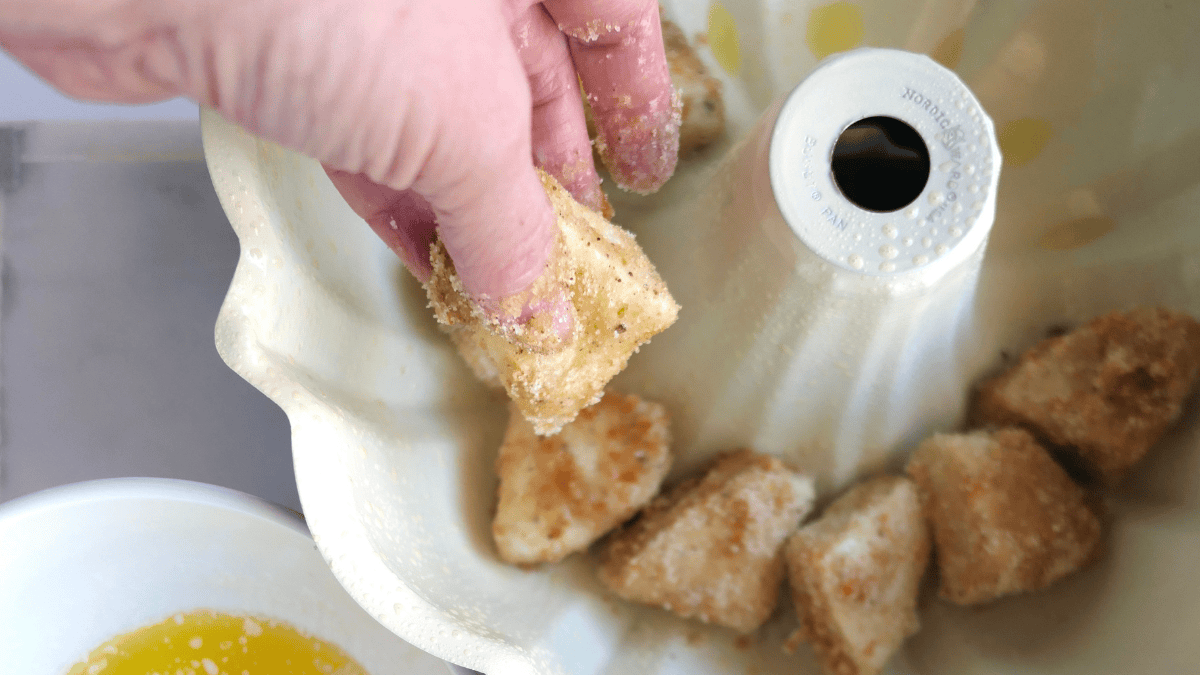 Hand placing biscuit pieces into a bundt pan.