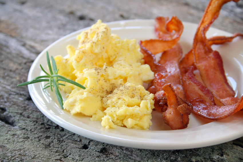 Scrambled eggs with crispy bacon on a plate, and garnished with a fresh sprig of Rosemary.