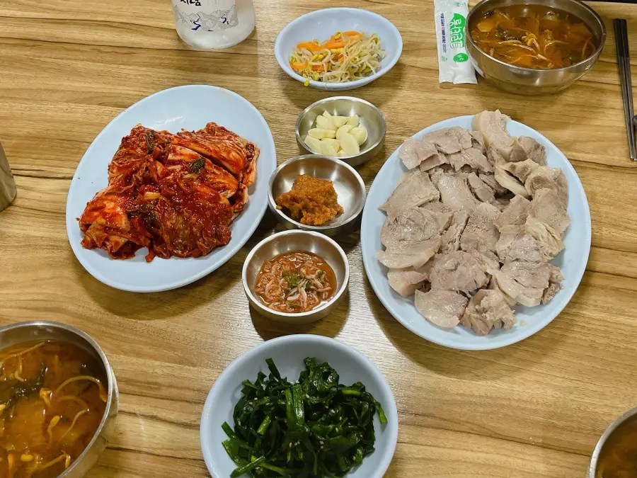수육, 김치, 마늘, 쌈장, 새우젓, 국과 반찬이 차려진 테이블 상차림