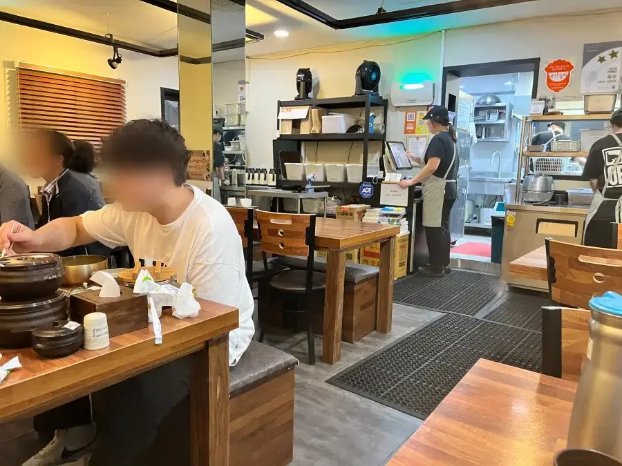 나무 테이블과 의자가 놓인 식당 내부에서 손님들이 식사를 하고 있는 모습.