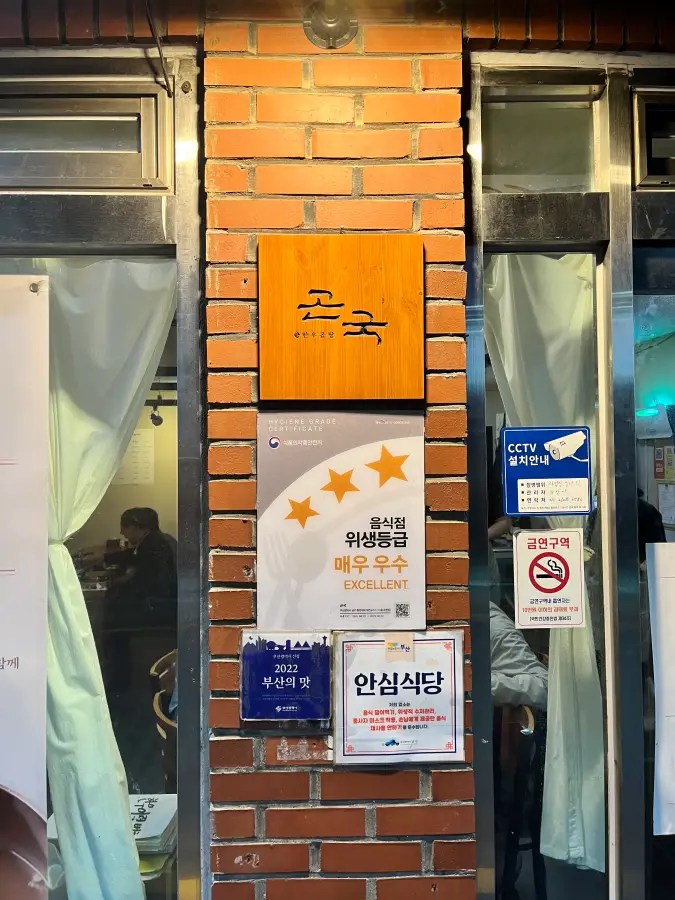식당 입구 벽면에 곤국 나무 간판과 위생등급 매우 우수 표지판이 붙어 있다.
