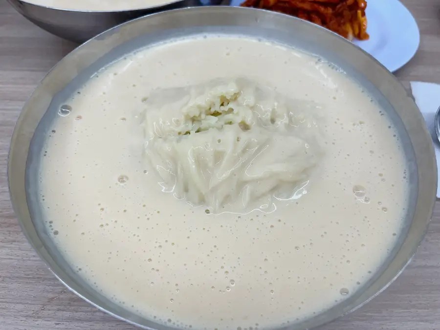 스테인리스 그릇에 뽀얗고 진한 콩국물과 면이 담겨 있는 냉콩국수이다.