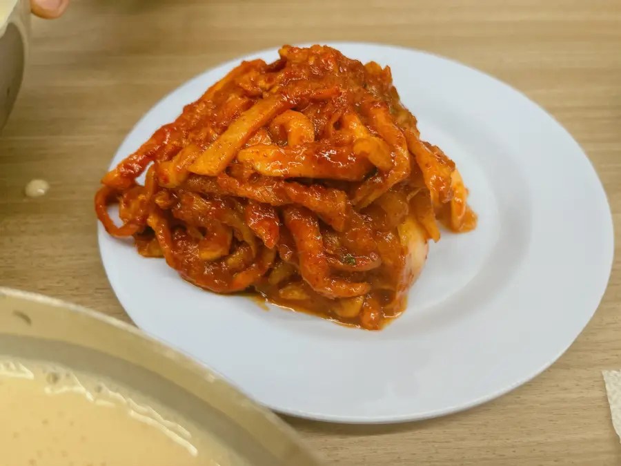 하얀 둥근 접시 위에 붉은 양념에 버무려진 무김치가 수북하게 쌓여 있다.