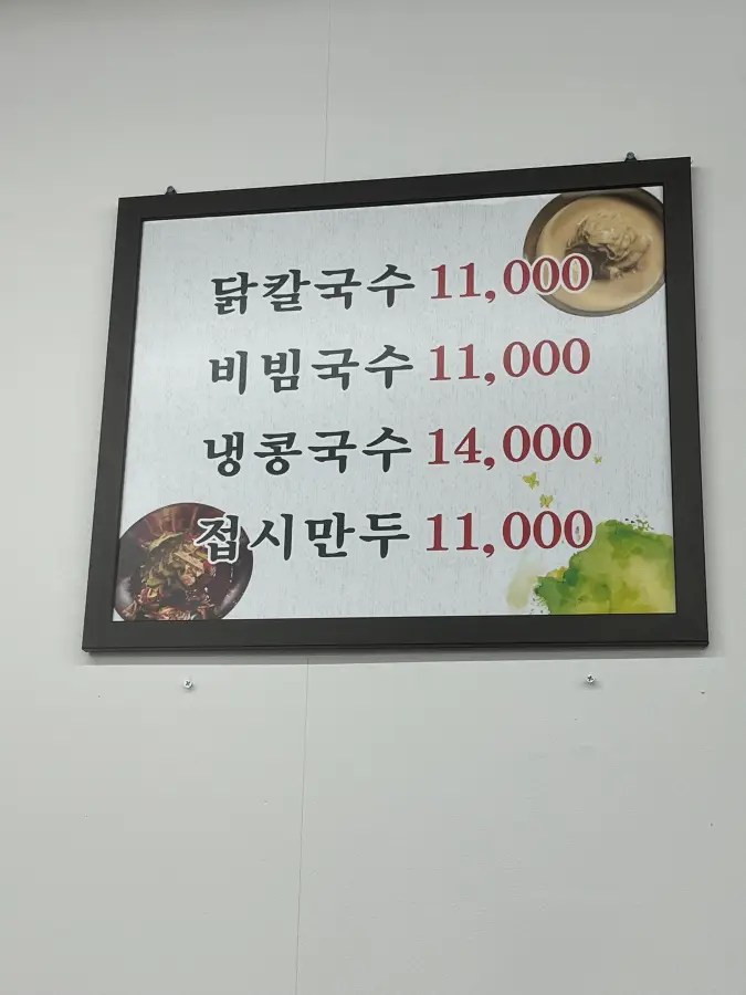 하얀 벽에 닭칼국수, 비빔국수, 냉콩국수, 접시만두의 가격이 적힌 메뉴판이 걸려 있다.