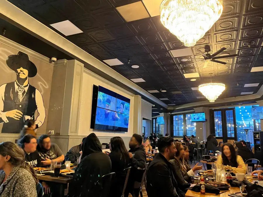 Personas cenando en el interior de un restaurante decorado con un mural de vaqueros y un candelabro.