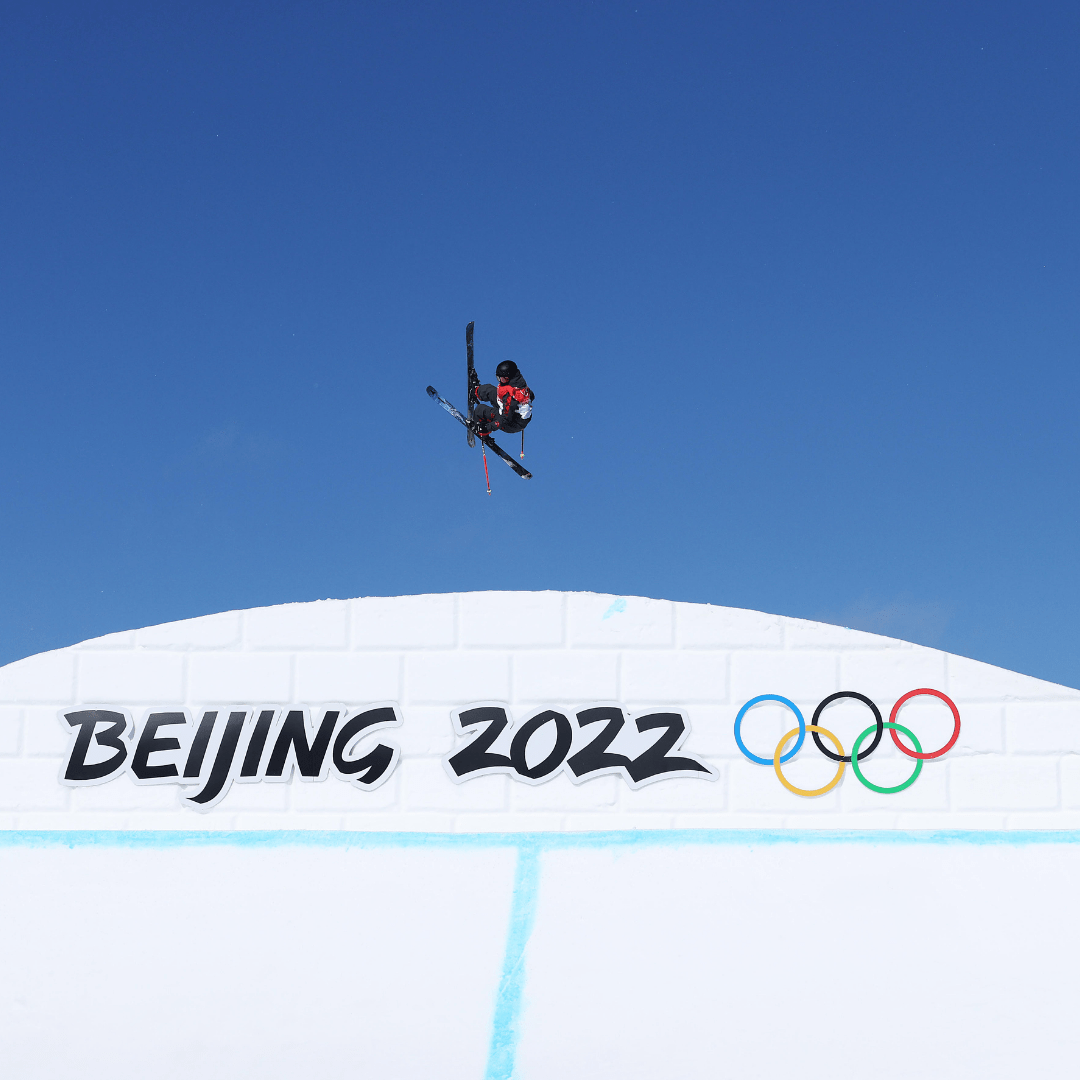 Megan Oldham doing a ski jump over a white hill with "Beijing 2022" written on it, with a Olympic logo on the right.
