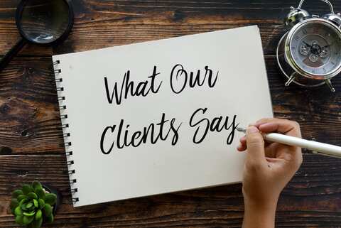 Notebook reading What Our Clients Say beside a clock and magnifying glass