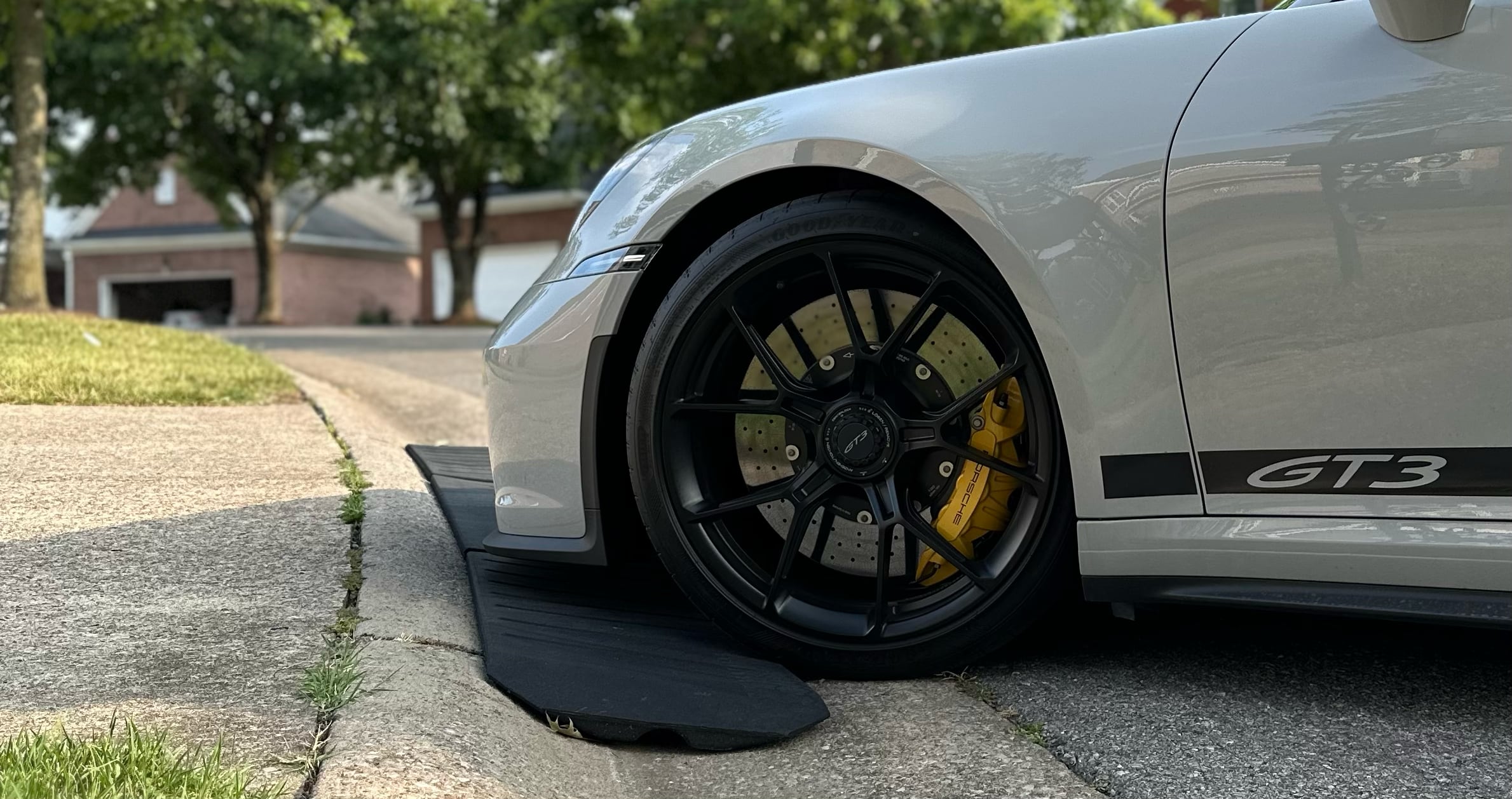 Front wheel of a white Porsche GT3 on a Smooth Curb rubber ramp at a driveway curb