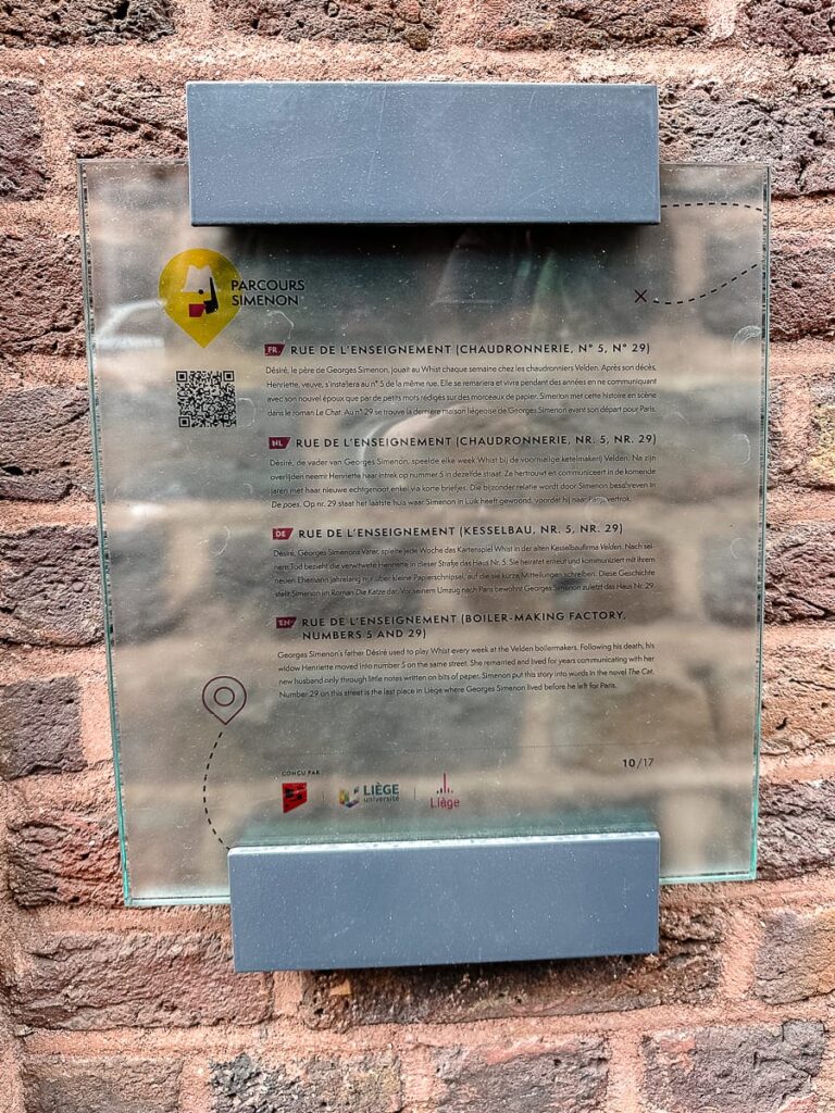 Kleines Hinweisschild zum Parcours Simenon an einer Punkt auf der Tour, durchsichtig, Texte in vier Sprache, QR-Code.
