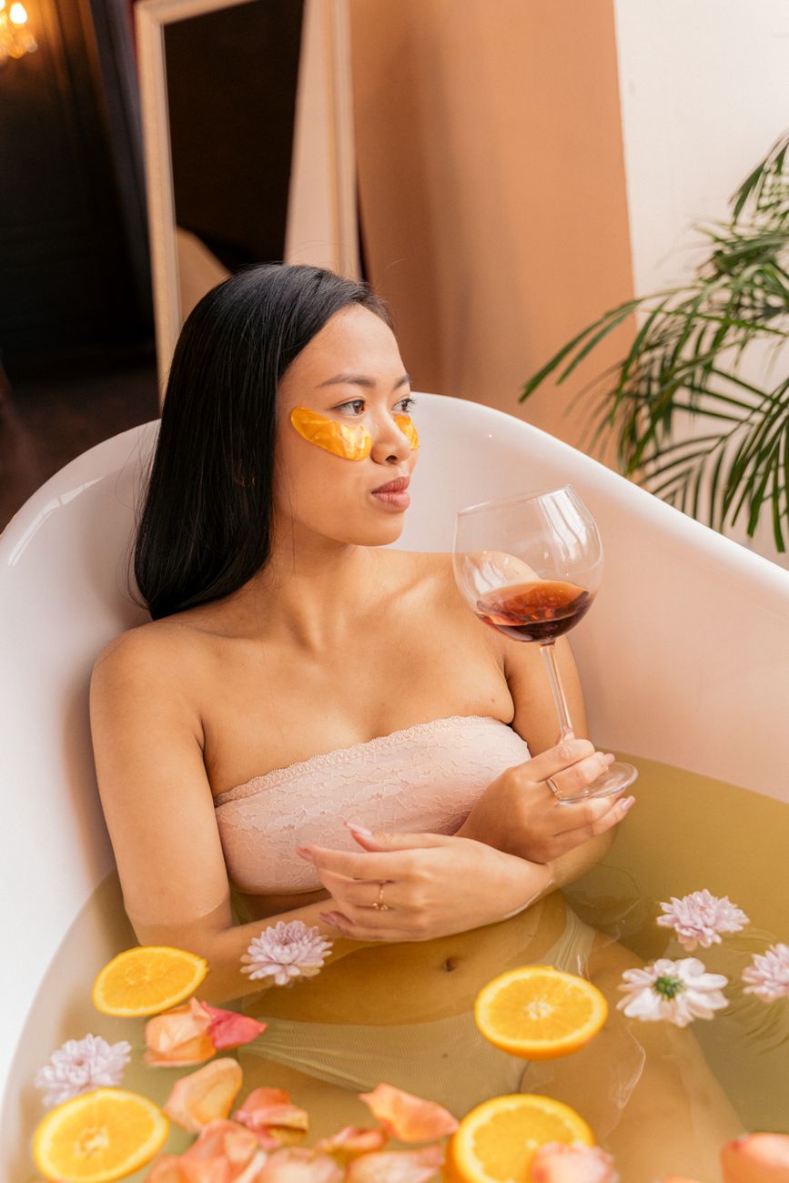 woman with a wine glass and a face mask relaxing in a bathtub