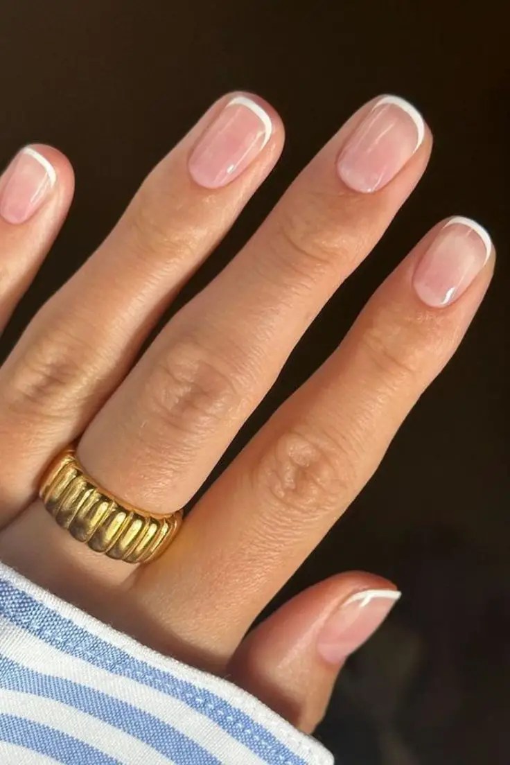 Short natural nails with thin white micro French tips and a glossy nude base.