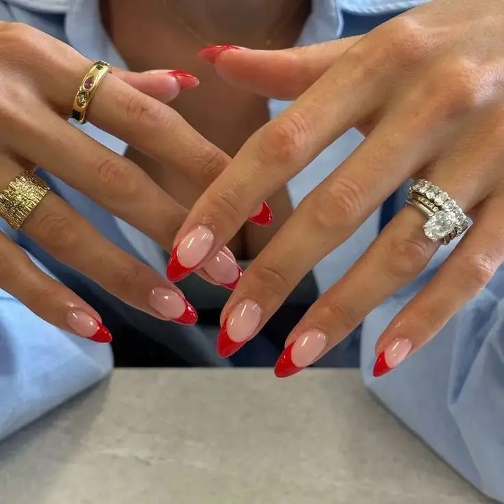 Almond-shaped nude nails with glossy red French tips on both hands.