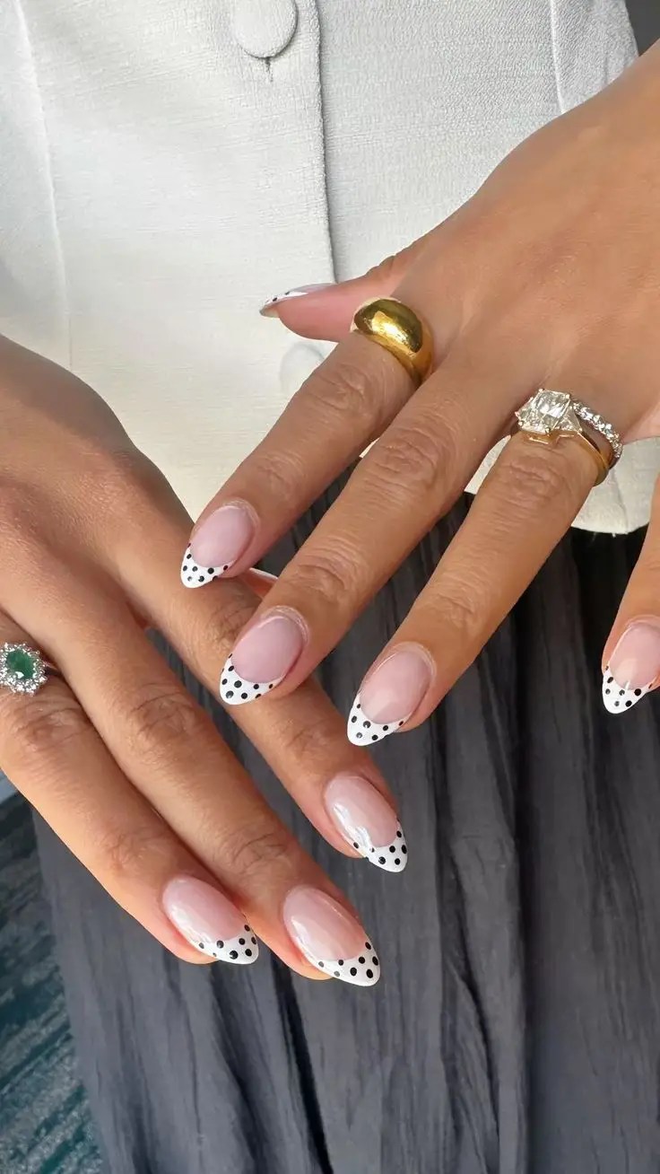 Nude almond nails with white French tips decorated with small black polka dots.
