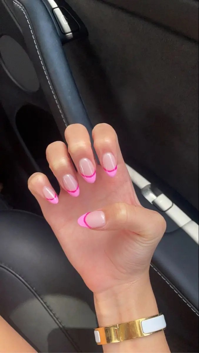 Short rounded nails with neon pink French tips over a sheer nude base.