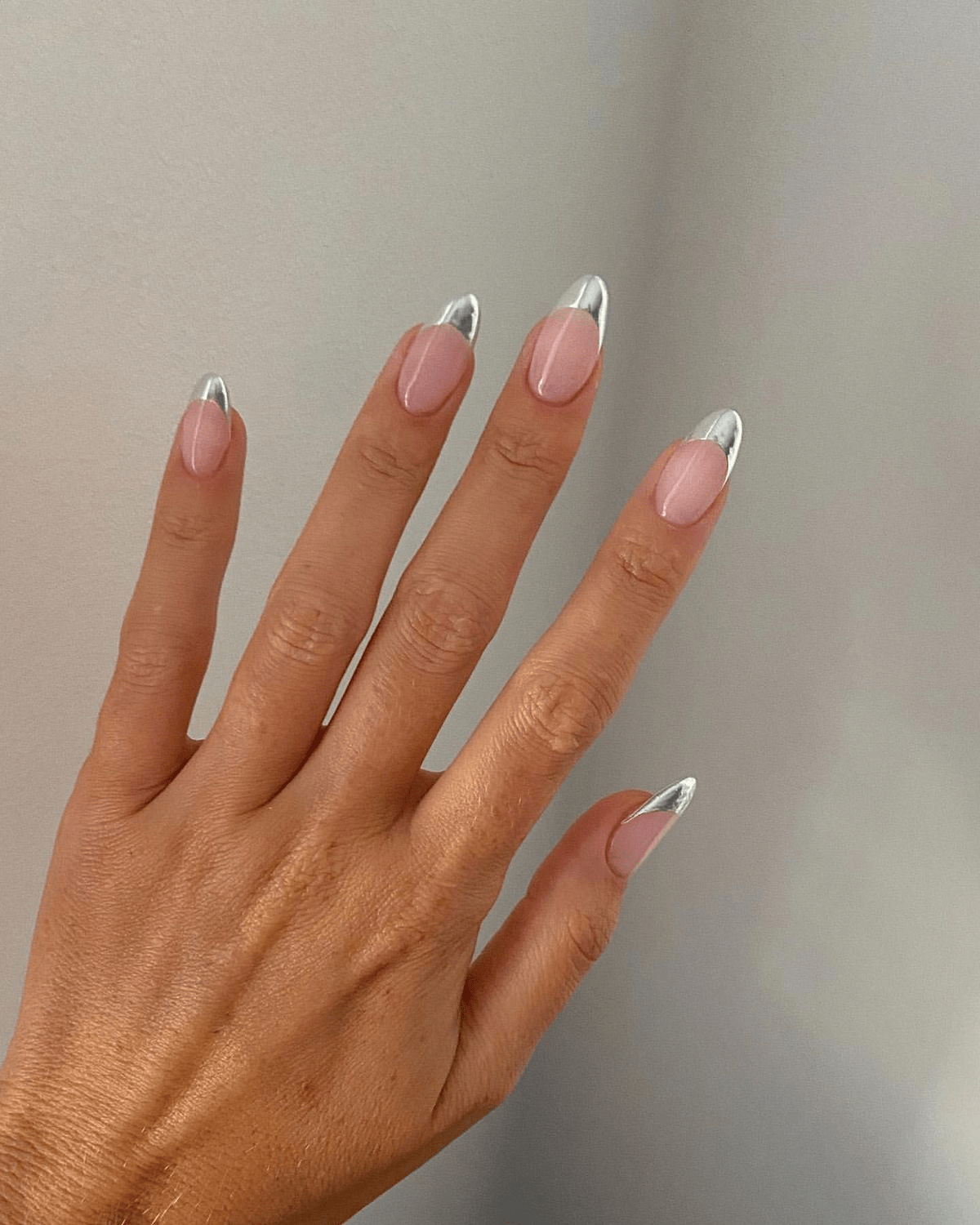 Almond nude nails with reflective silver chrome French tips.