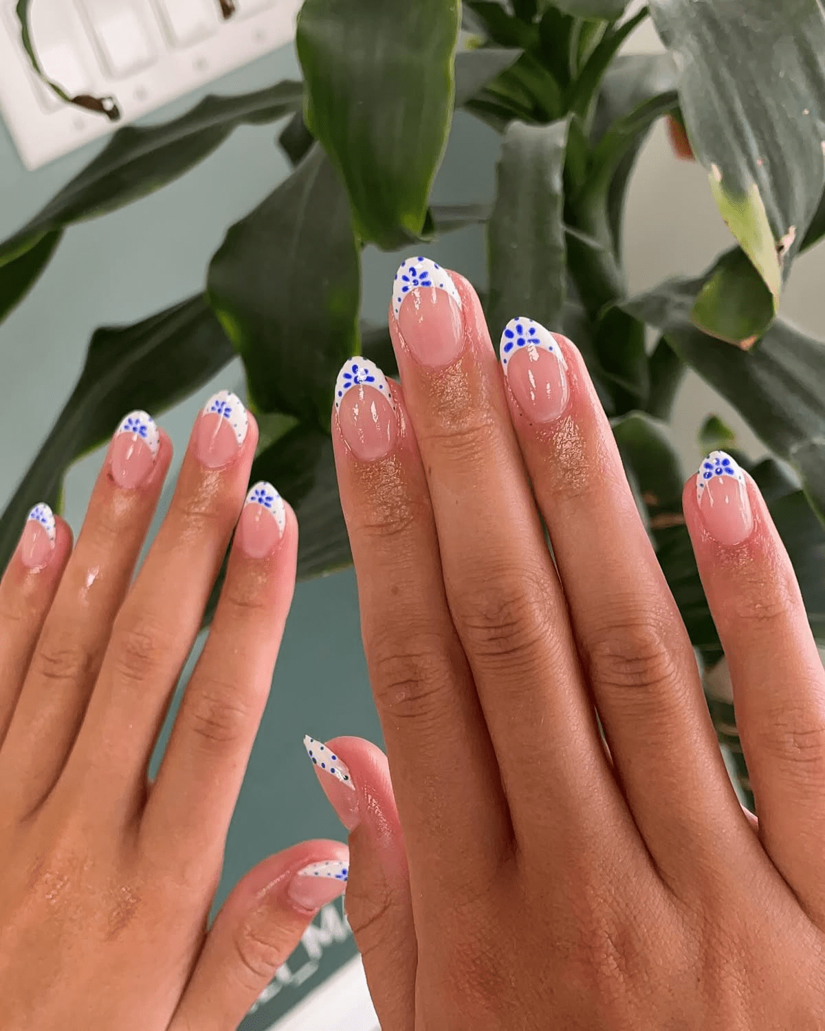 Short nude nails with white French tips decorated with small blue floral designs.