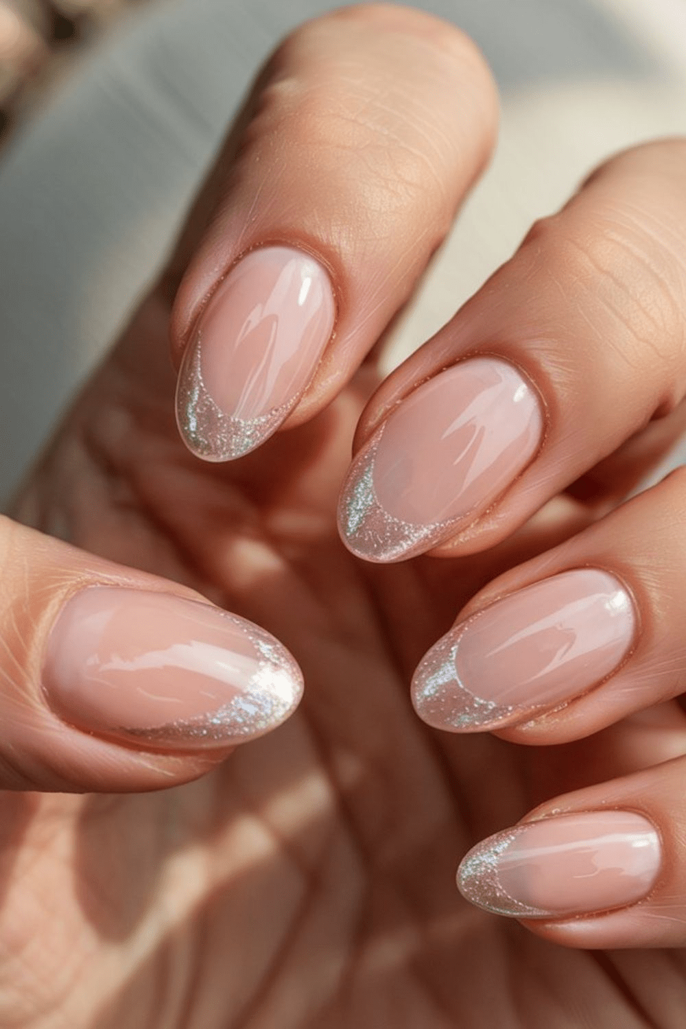 Almond nude nails with soft silver glitter French tips.