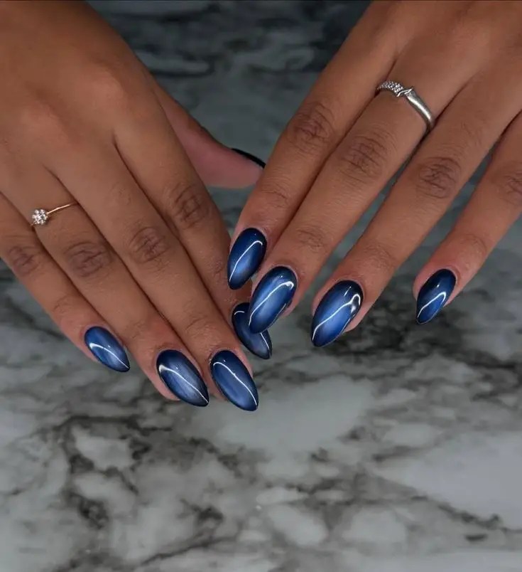 Dark navy almond nails with a bright magnetic blue cat eye streak.