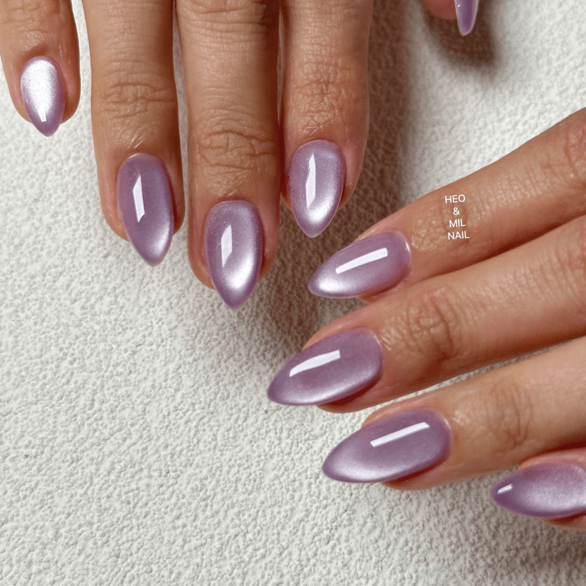 Shimmery lavender cat eye almond nails with a bright magnetic center glow.