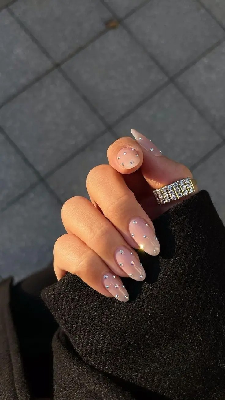 Nude almond nails decorated with small rhinestones placed evenly across each nail.