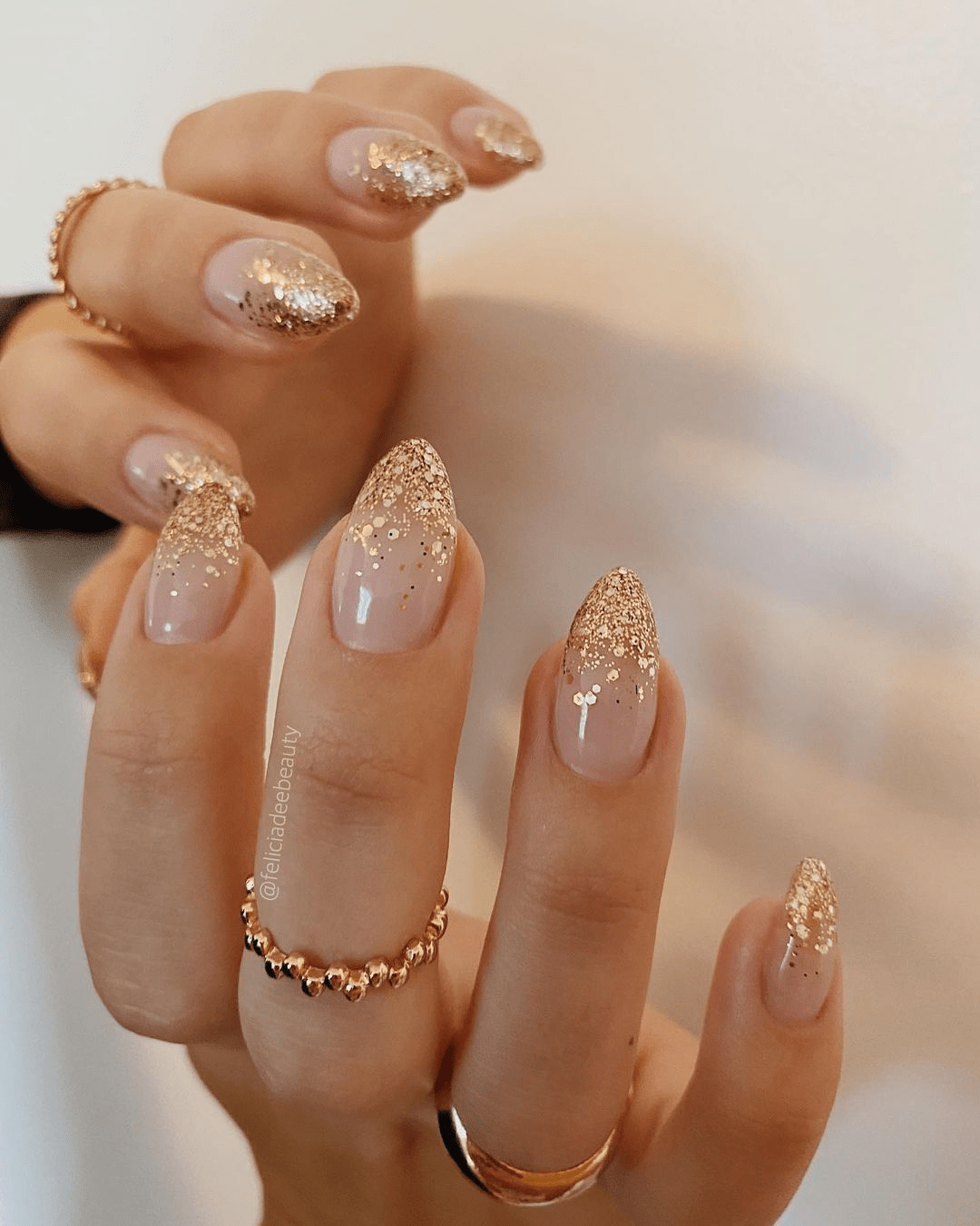Nude almond nails with dense gold glitter fading softly from the tips.