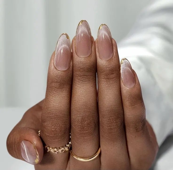 Shimmery nude nails with thin metallic gold accents along the edges and tips.