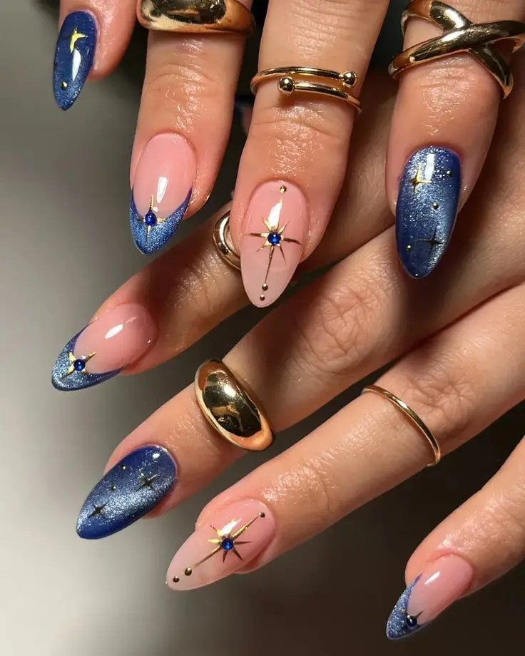 Blue cat-eye nails paired with nude nails featuring gold starburst accents and blue rhinestones.