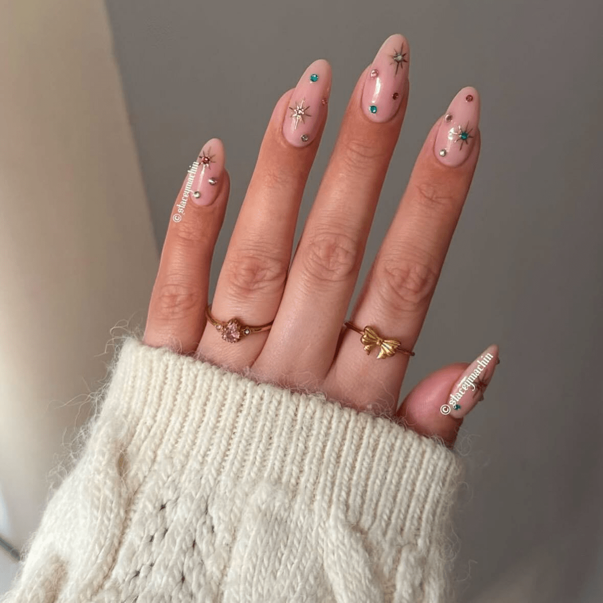 Nude almond nails decorated with multicolored rhinestones and gold starburst accents.