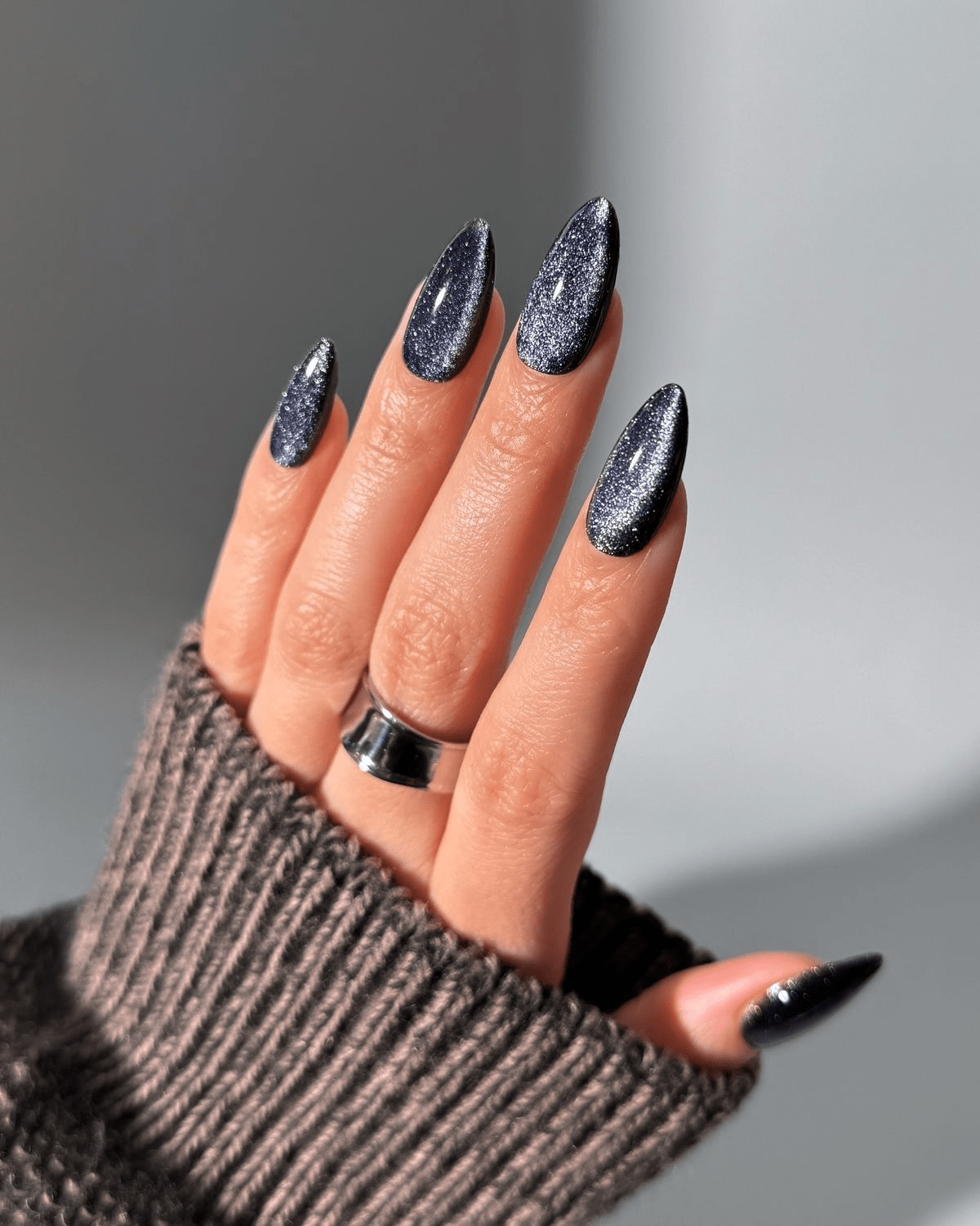 Navy glitter almond nails shining under bright light.