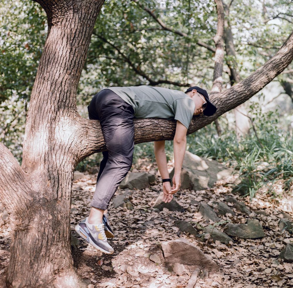 man in black t-shirt and blue denim jeans sitting on tree branch