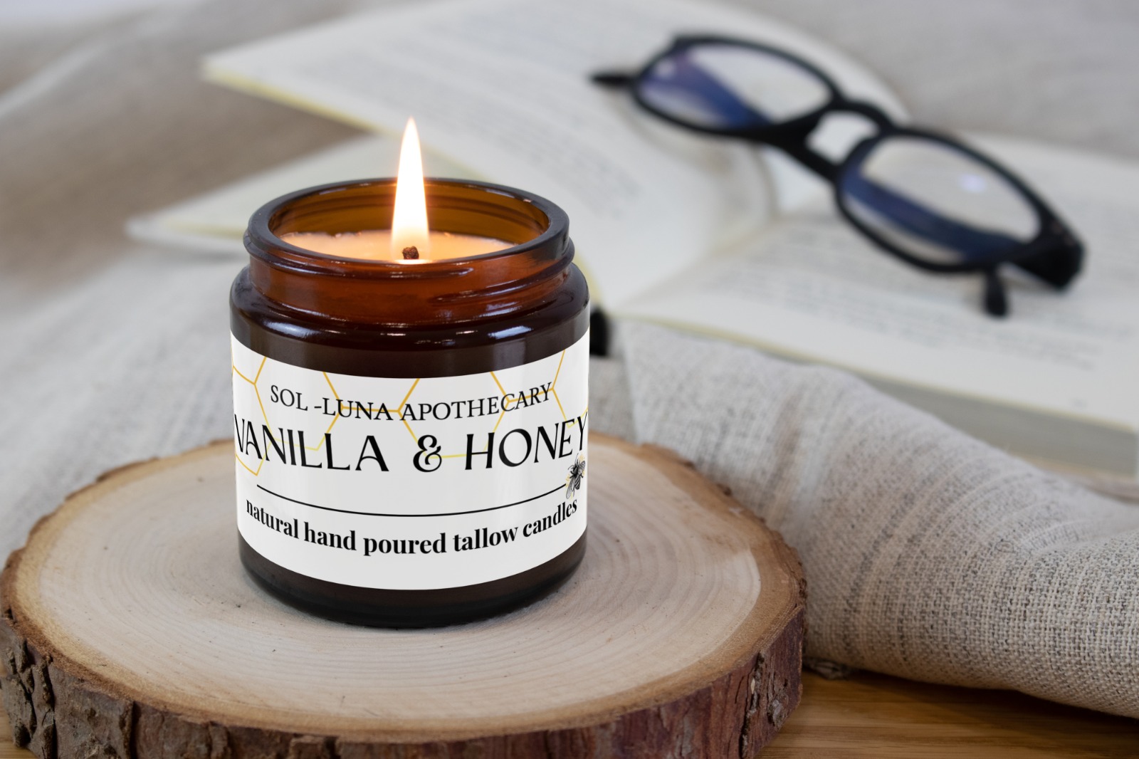 picture of a candle with vanilla & honey written on it sitting on a piece of log in front of some papers and reading glasses