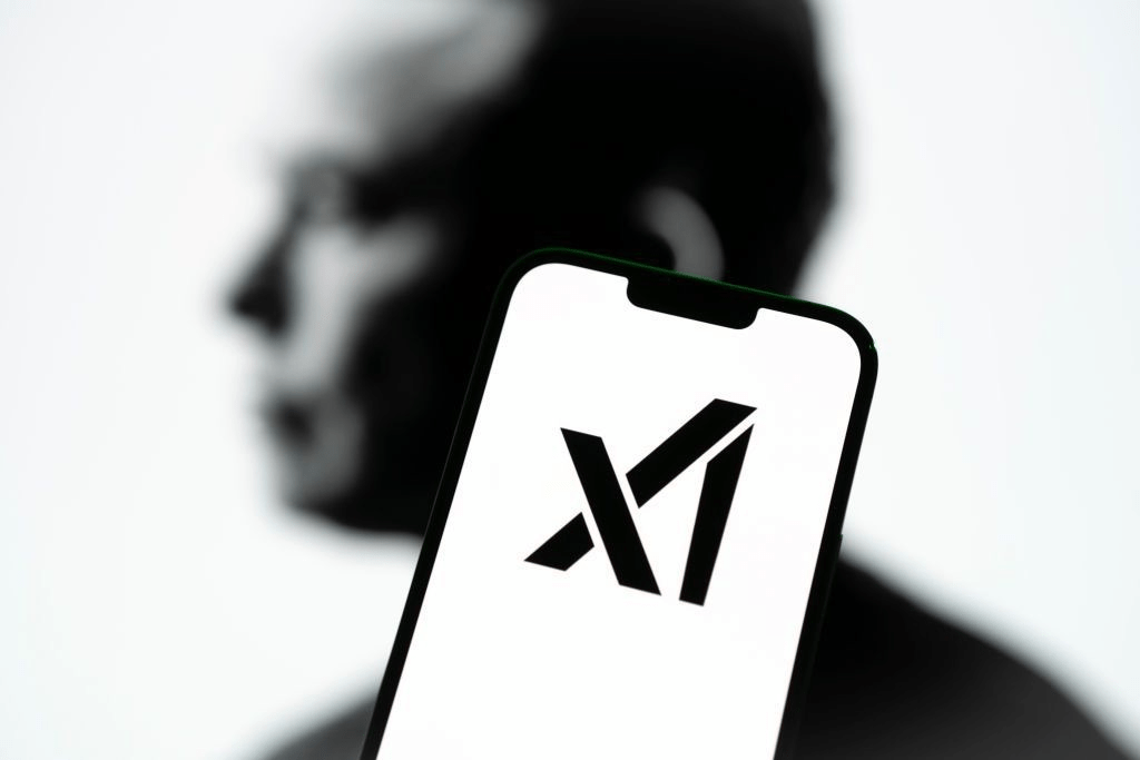 A smartphone displays the xAI logo, with a blurred silhouette of a person in the background.
