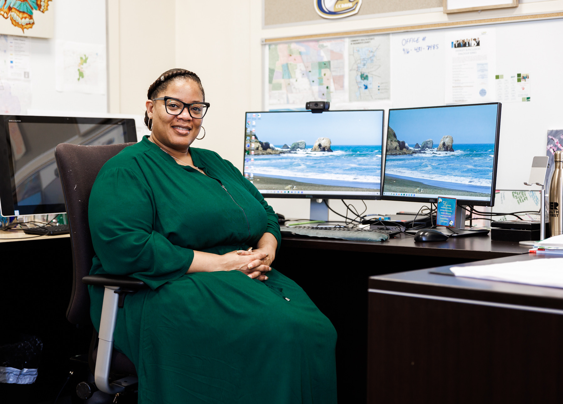 A woman sits at a desk with three computer screens behind her.