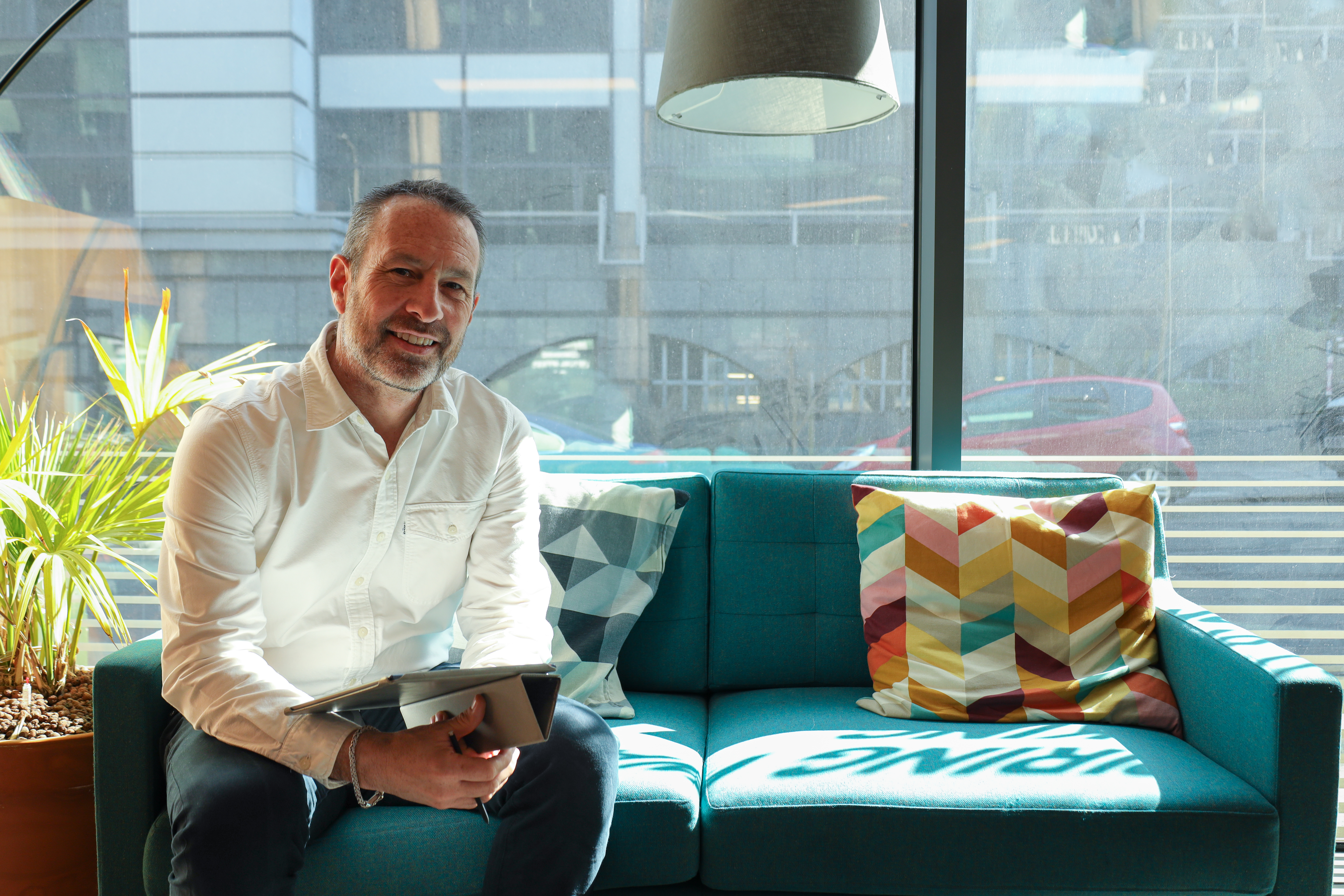 Interviewee sat on a sofa facing and smiling to the camera, ready to be interviewed