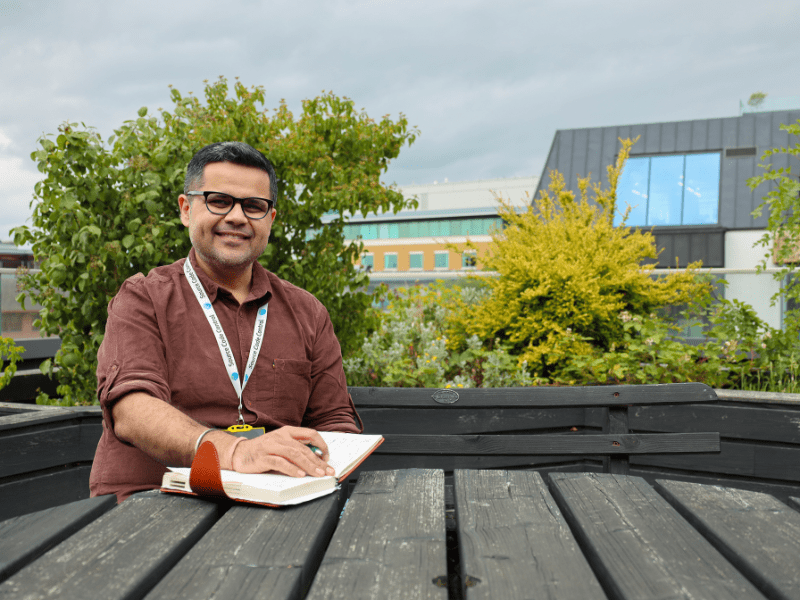 A picture of Source Code Control's New FinOps Lead, Abhinav Sarna, sat on a bench with his notepad, ready for the interview